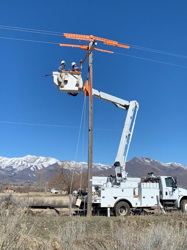 Line crews lifted in a boom working on a power line pole.